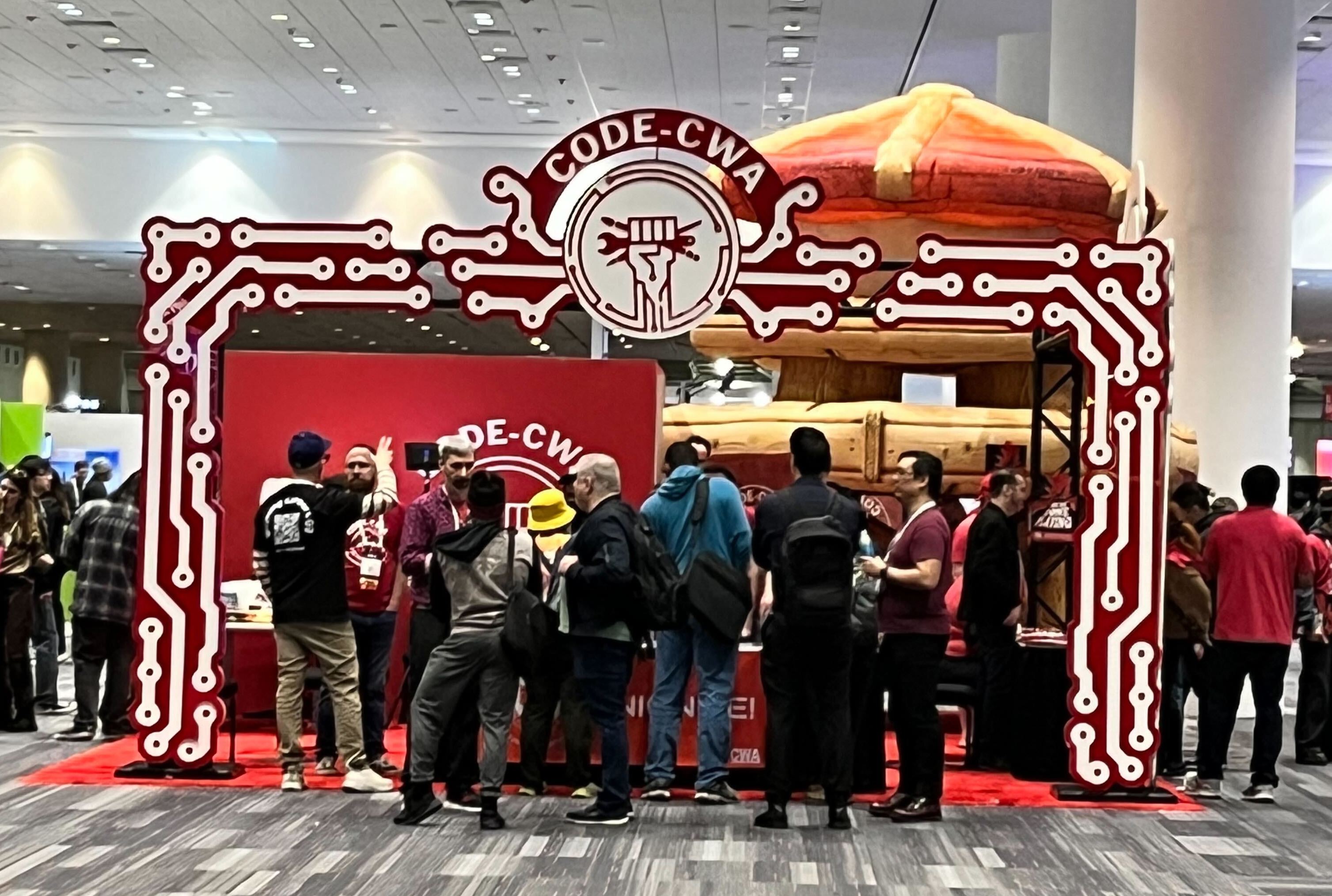 The CWA booth at GDC 2025, decorated with red and white circuits. People are standing at the entrance to the booth, and above their heads is the CODE-CWA logo.